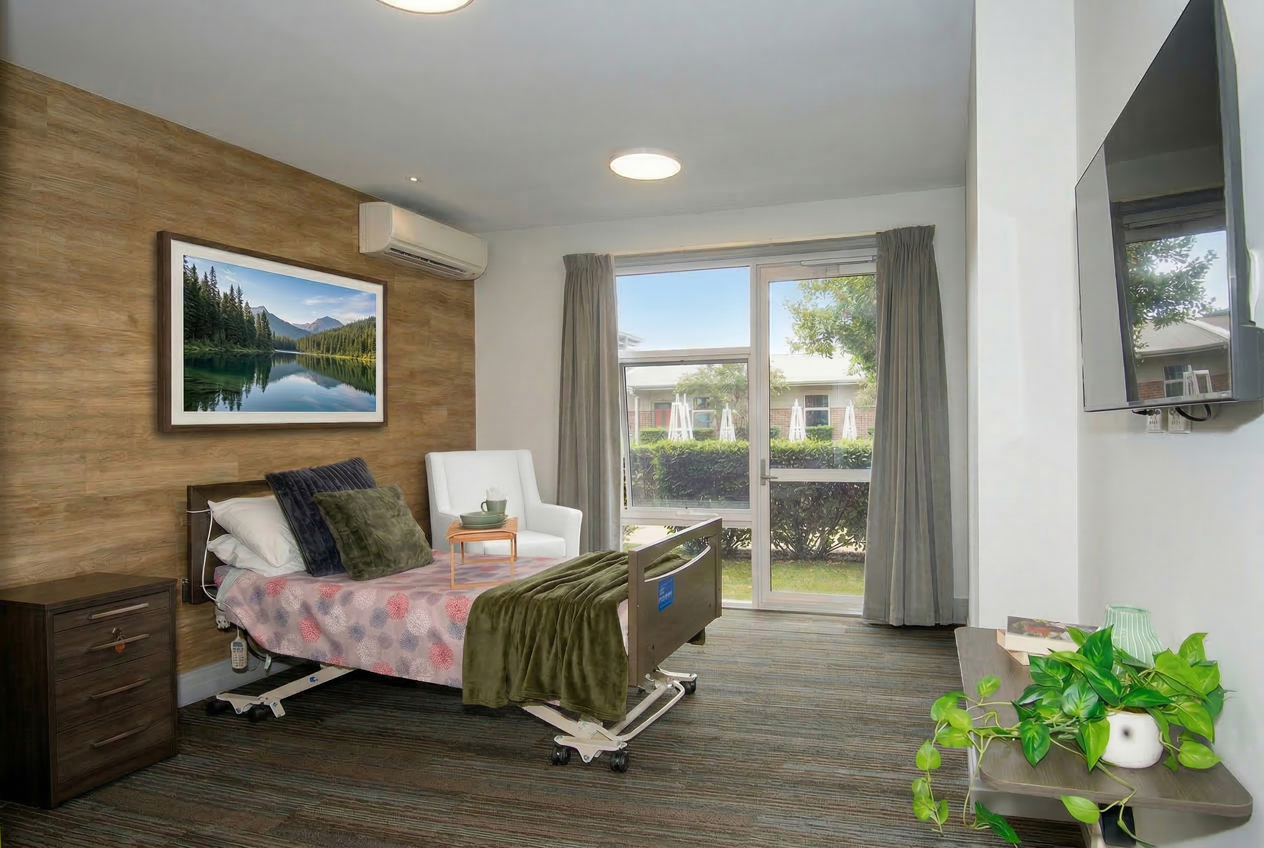 A modern Burpengary Manor Aged Care deluxe room featuring patio access, landscaped garden views, and a wall-mounted Smart TV.
