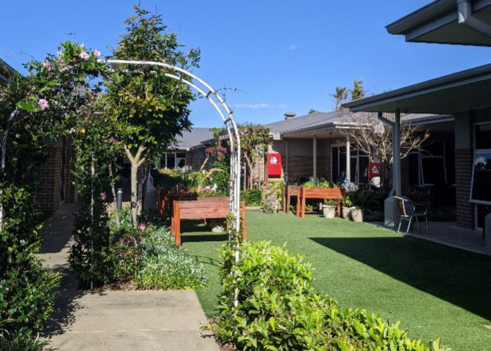 A bright garden courtyard at Burpengary Manor Aged Care with flower arches, green lawns, and accessible walking paths.